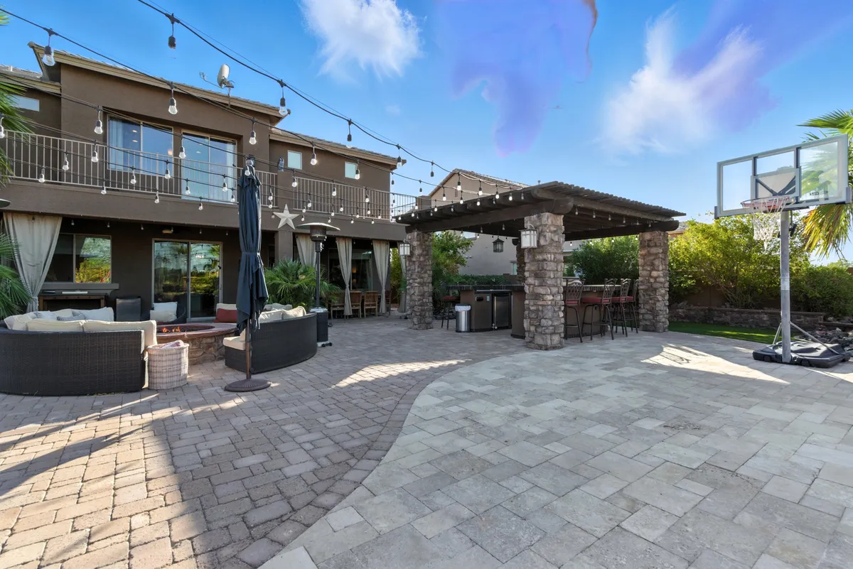 A relaxed outdoor seating area featuring a pergola for shade, comfortable chairs, and a basketball hoop set against a backdrop of desert landscaping. The space is clearly designed for outdoor dining, socializing, and enjoying group activities.