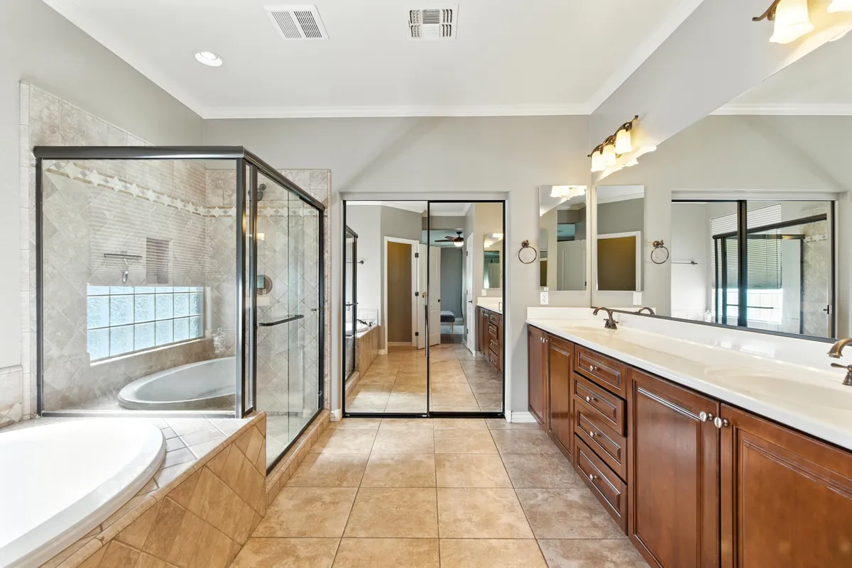 A luxurious bathroom with a double sink vanity, glass shower enclosure, soaking tub, and large mirrors. The scene suggests relaxation and self-care in a serene and sophisticated setting.