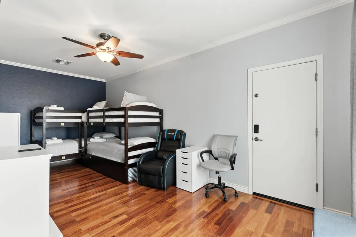 A practical and welcoming bunk room showcasing bunk beds, an ergonomic chair at a desk area, and warm wooden flooring. The space is designed for both sleep and productivity, ideal for families or groups traveling with kids or teens.