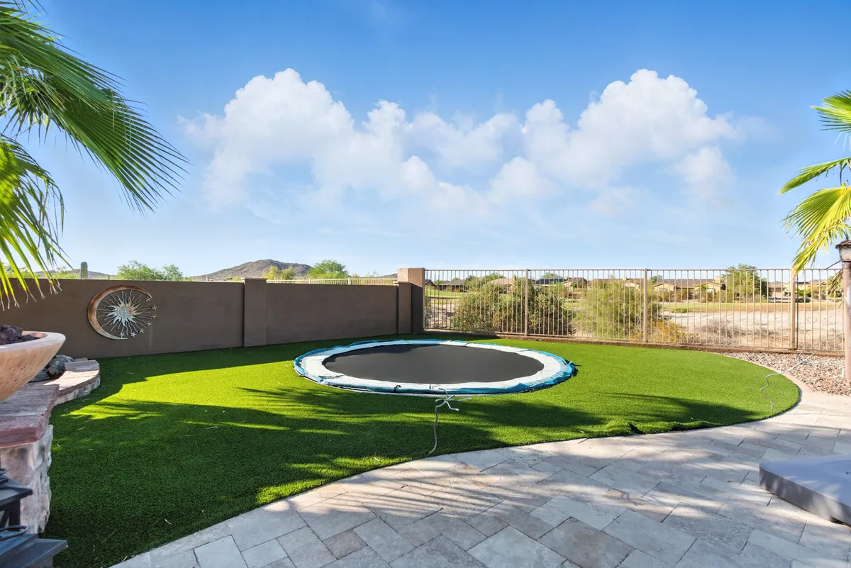 A playful, landscaped backyard with an in-ground trampoline, grassy area, and artistic wall feature, designed for outdoor activities and family gatherings. The vibrant setting encourages active play and lasting memories.
