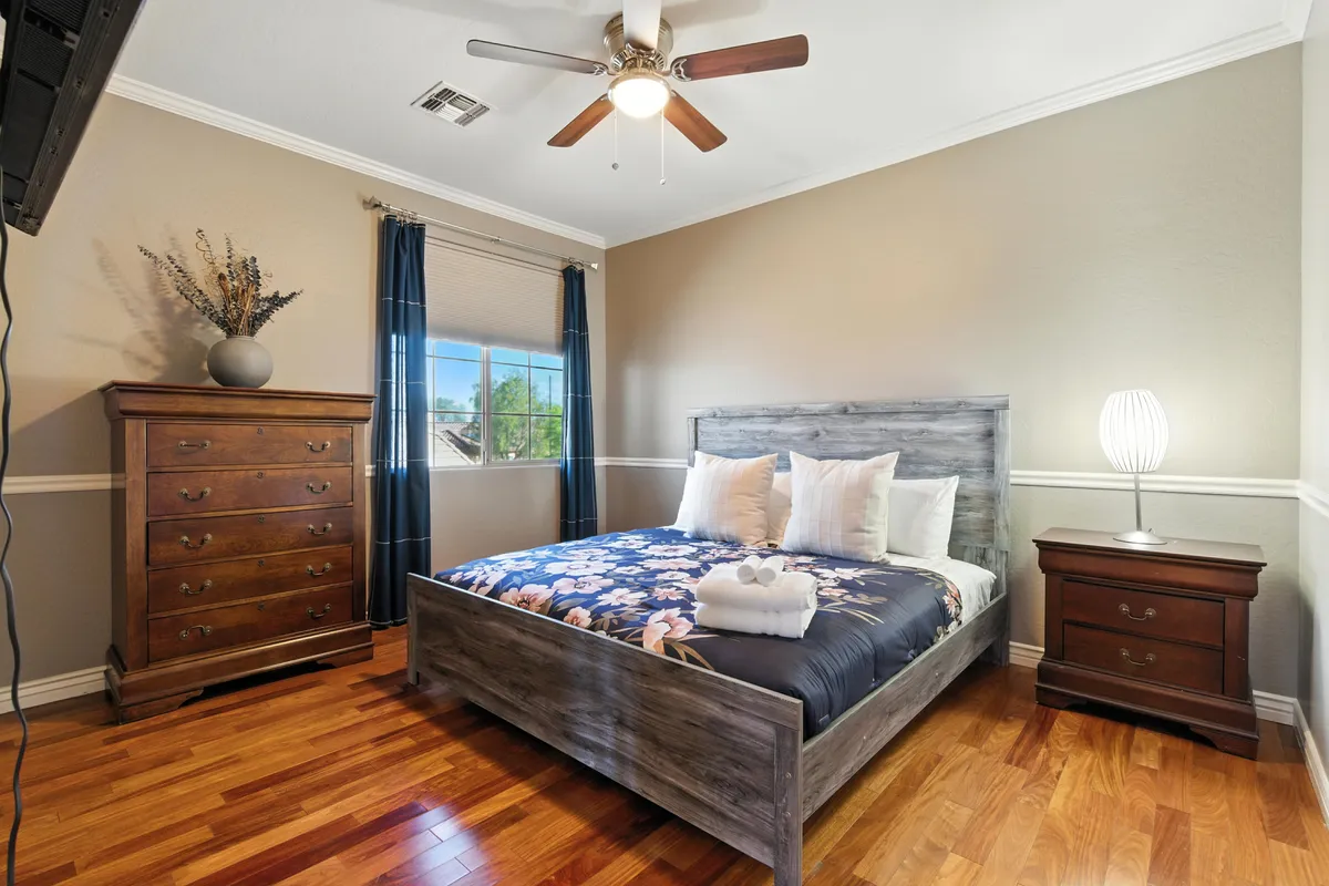 A serene bedroom featuring a bed with floral bedding, a wooden dresser, a nightstand with a lamp, and a window with curtains softly letting in natural light. The overall mood is calm and tranquil, emphasizing comfort and restful sleep.