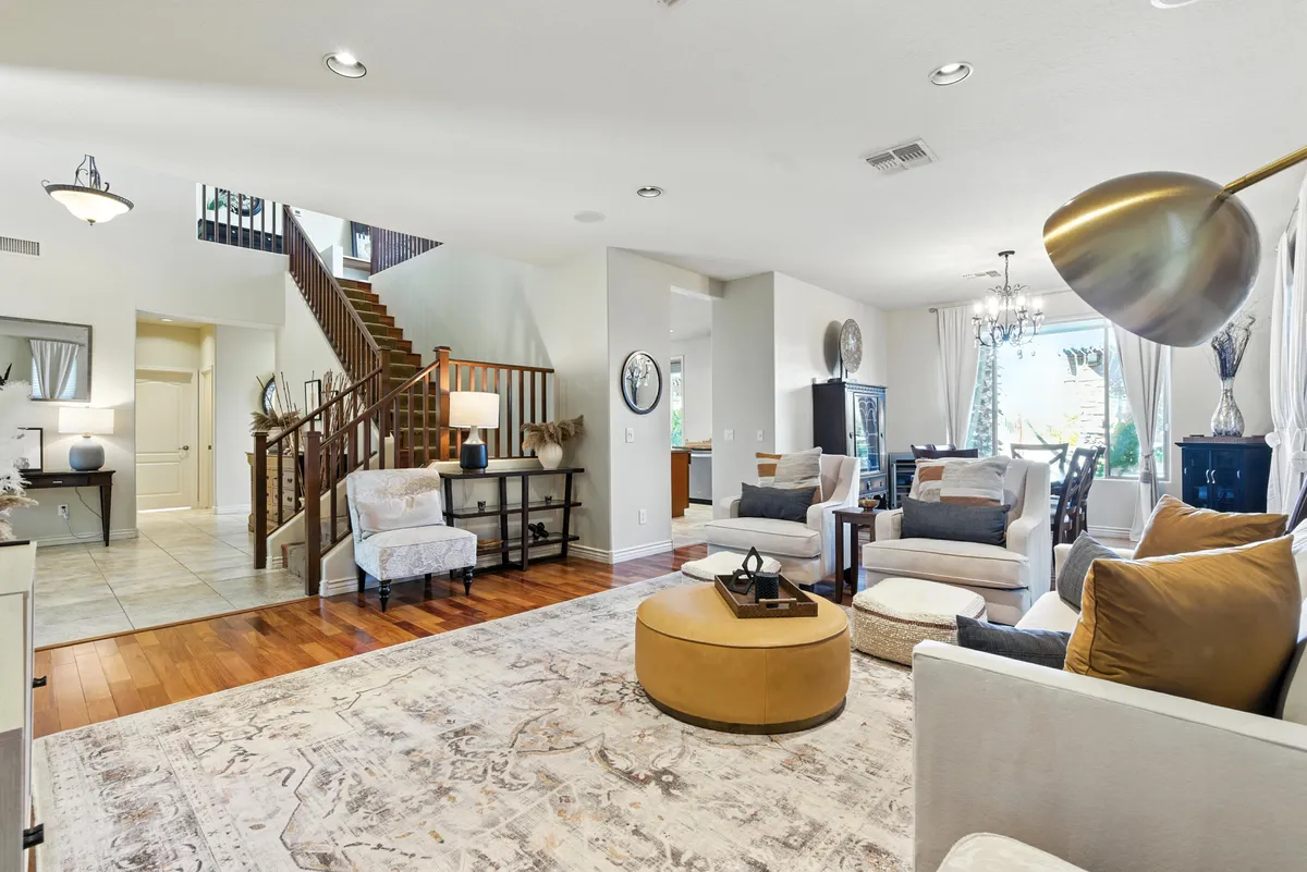 A spacious and inviting living room with a modern staircase, a large coffee table, a plush sectional sofa arranged for group gatherings, and decorative accents that add warmth. Natural light pours in, creating an uplifting and social atmosphere perfect for conversations and celebrations.