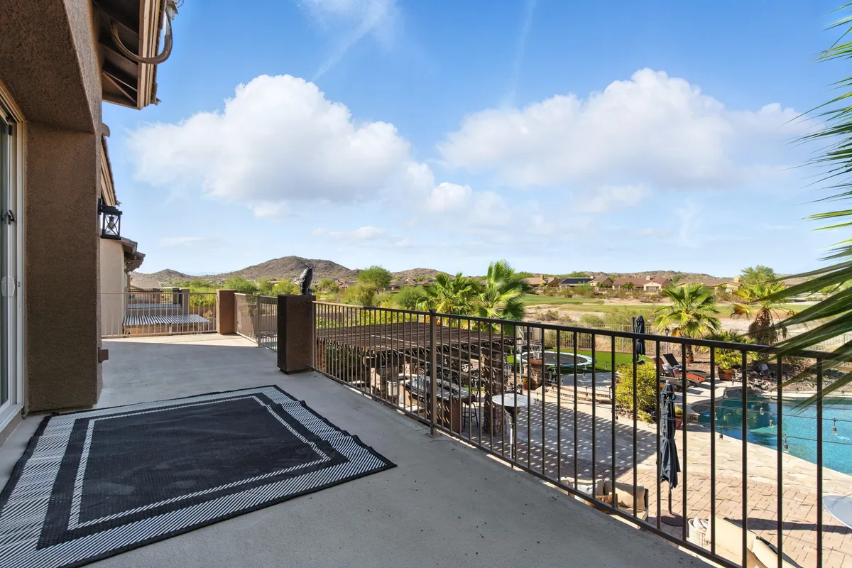 This exterior image captures a sun-filled balcony overlooking a sparkling swimming pool framed by palm trees and lush landscaping. The balcony features comfortable outdoor furniture, perfect for relaxing or informal group gatherings, and offers a tranquil view of the pool below, suggesting both relaxation and inspiration.
