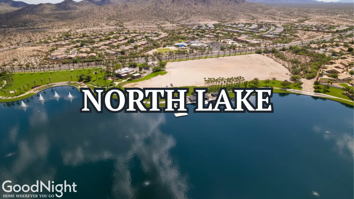 A scenic view of a serene lake with surrounding homes, landscaped green spaces, and a stunning mountain backdrop. The atmosphere is peaceful with hints of outdoor activity and community life.