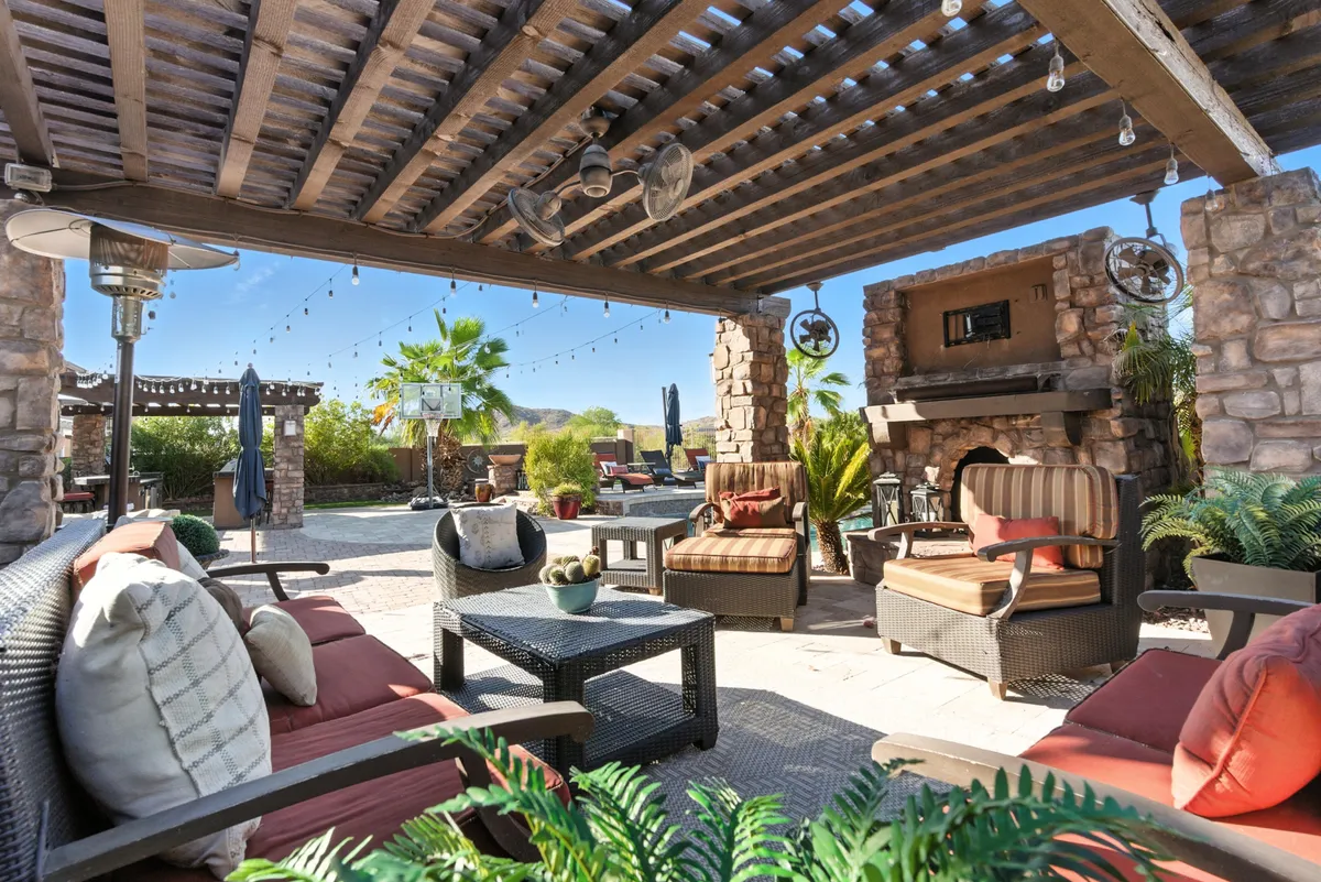 A cozy outdoor seating area arranged around a stone fireplace, with decorative plants and string lights overhead creating a warm, welcoming ambiance ideal for evening relaxation or gatherings.