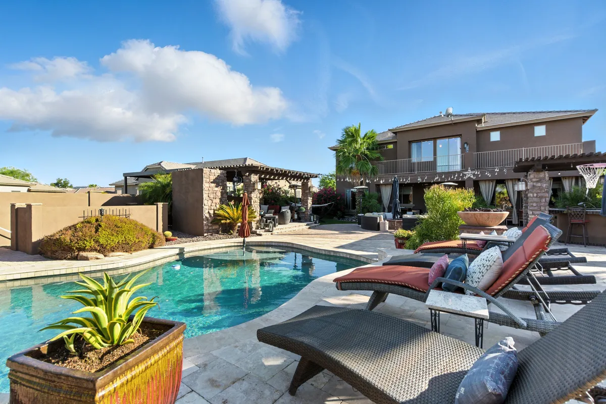 An inviting outdoor scene featuring a sparkling swimming pool surrounded by lounge chairs and lush greenery, with a comfortable outdoor seating area nearby. The setting is ideal for relaxing, sunbathing, or gathering with friends for lively conversation.